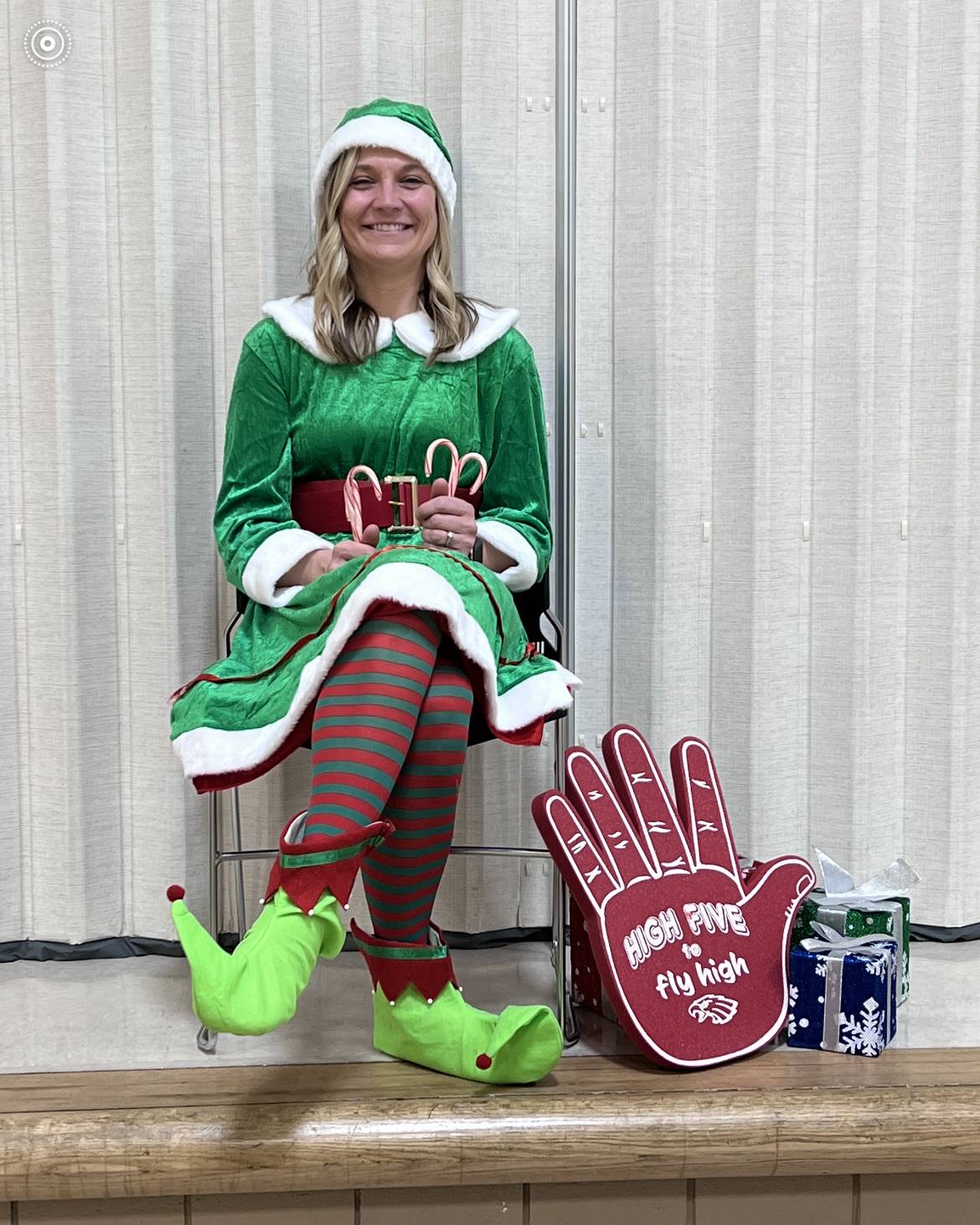Mrs. Heban, dressed in the elf costume, sits on the stage and greets students as they eat breakfast.