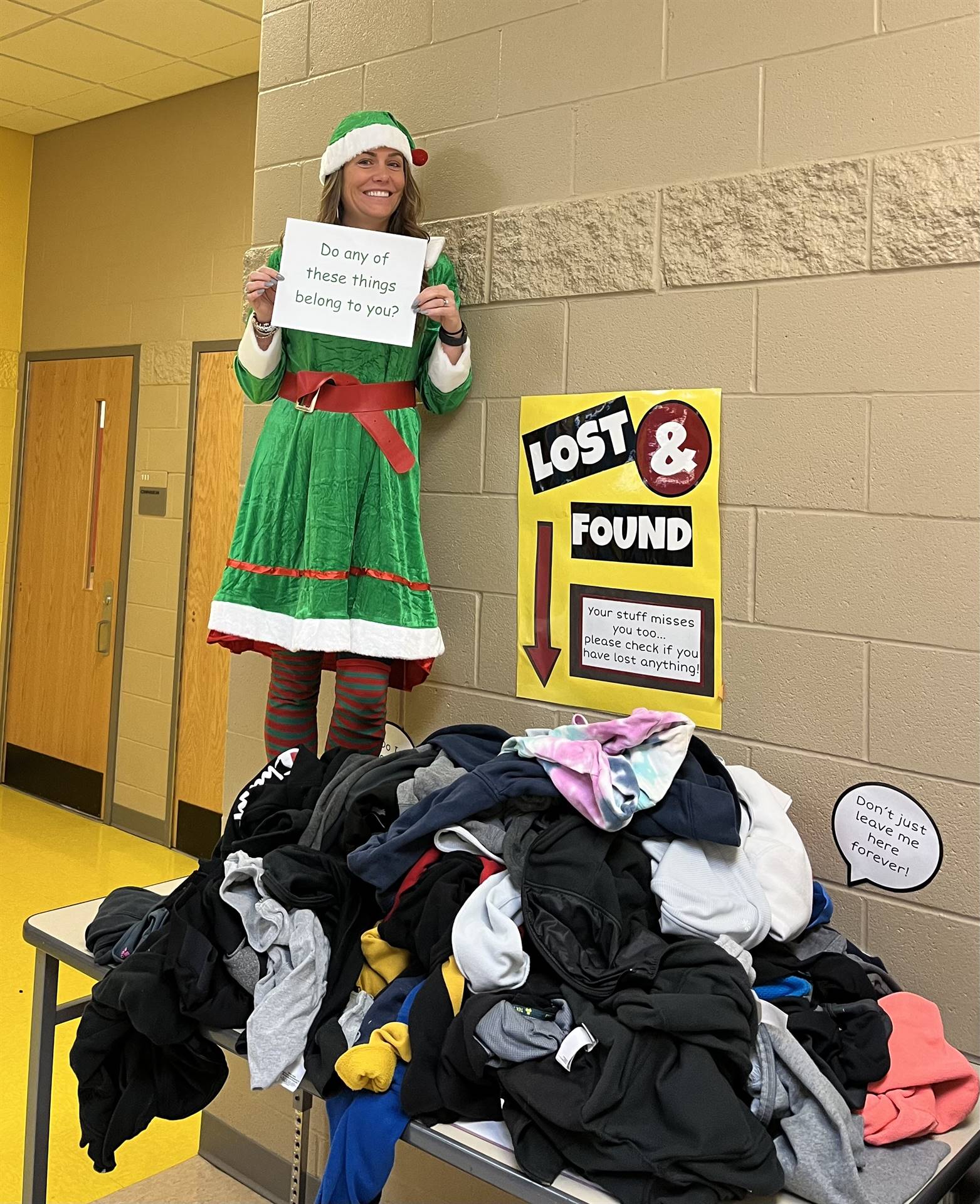 Principal Crawford dressed in elf costume standing on table holing a sign that reads "Does any of th