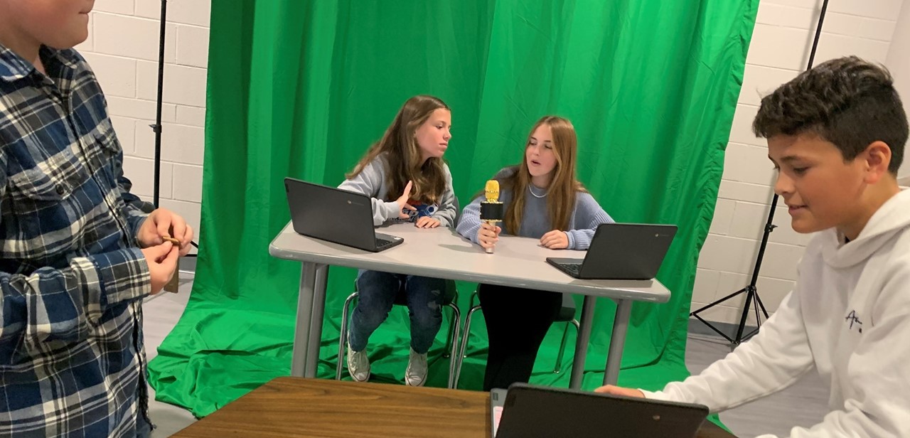Two students sitting at the news desk at the middle school