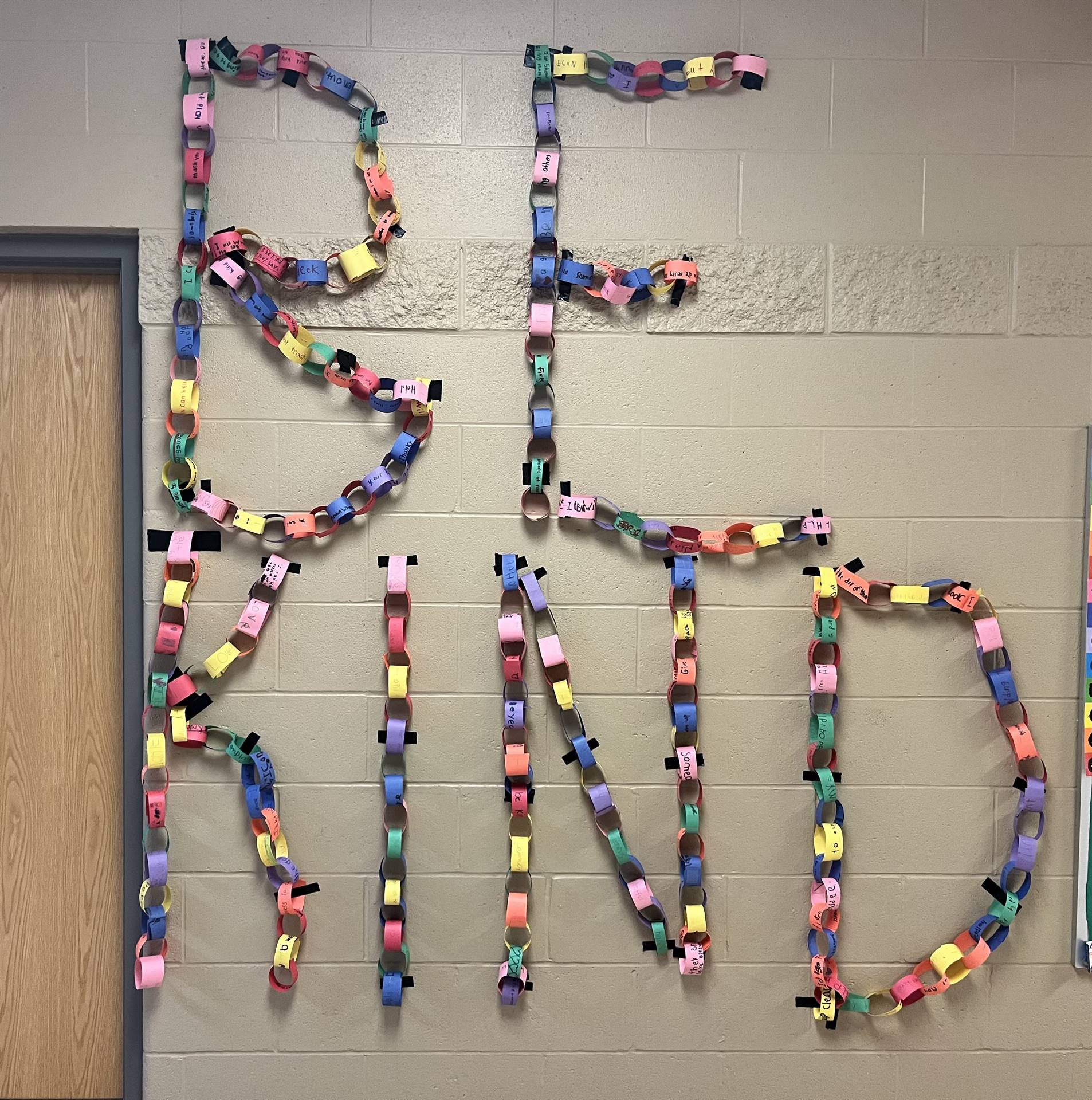 construction paper chain with multi colors that spell out "be kind" hanging on the wall