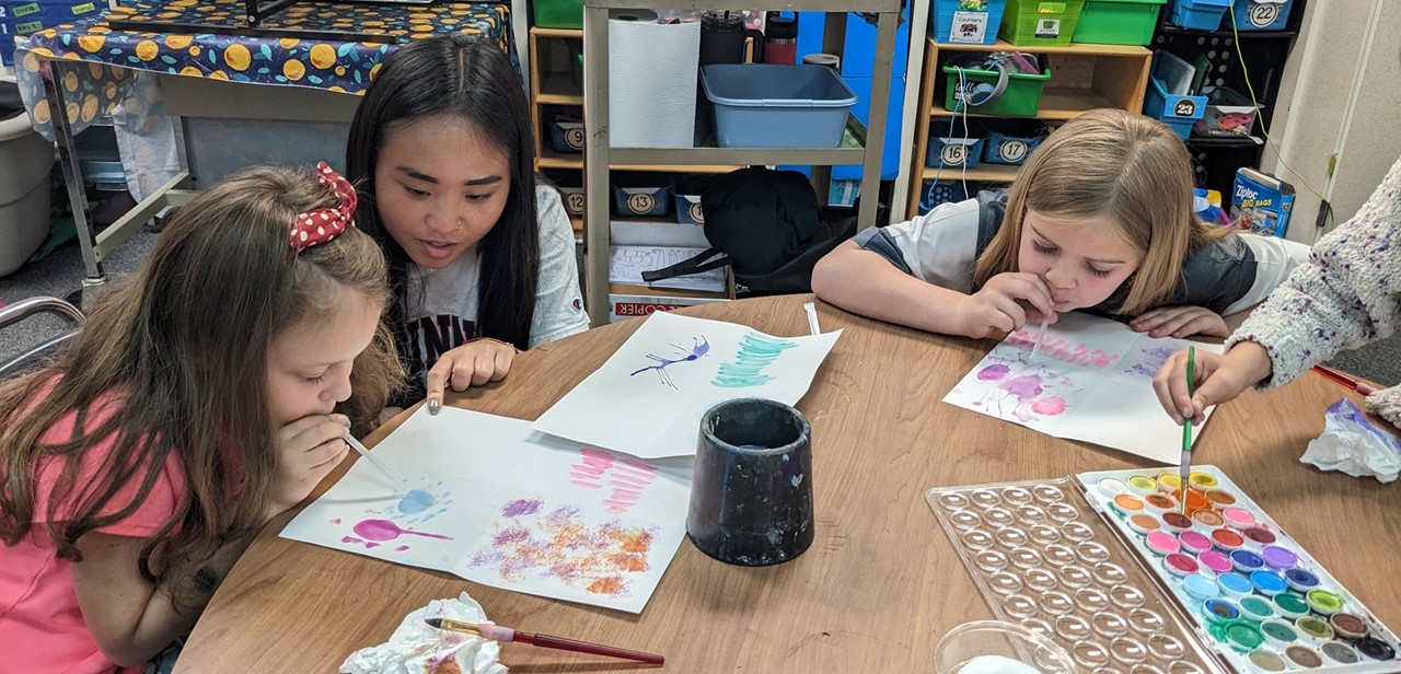 Art students using straws to blow paint across a page
