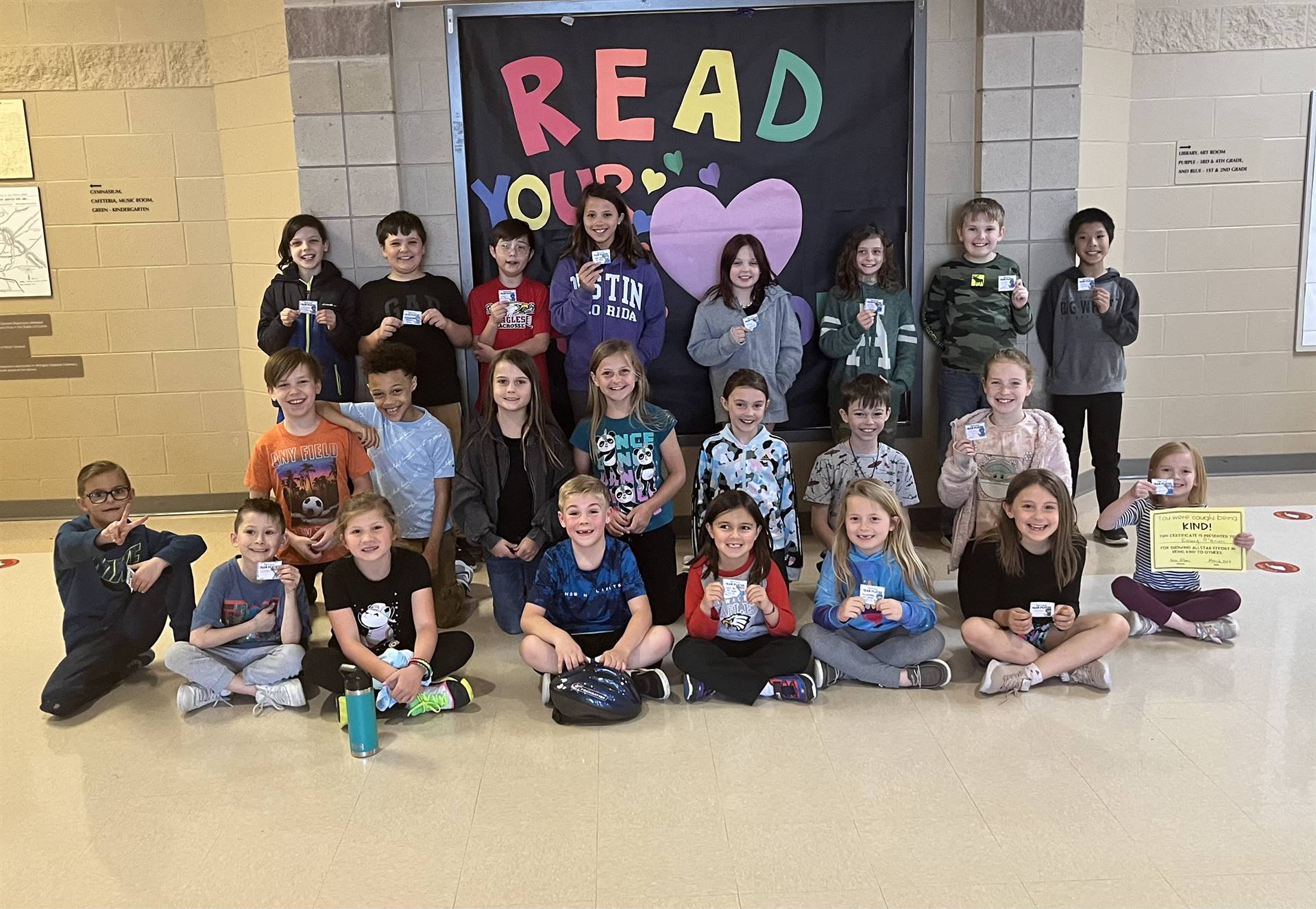 Group of approx 25 children grouped in front of a sign that reads "read your heart out"