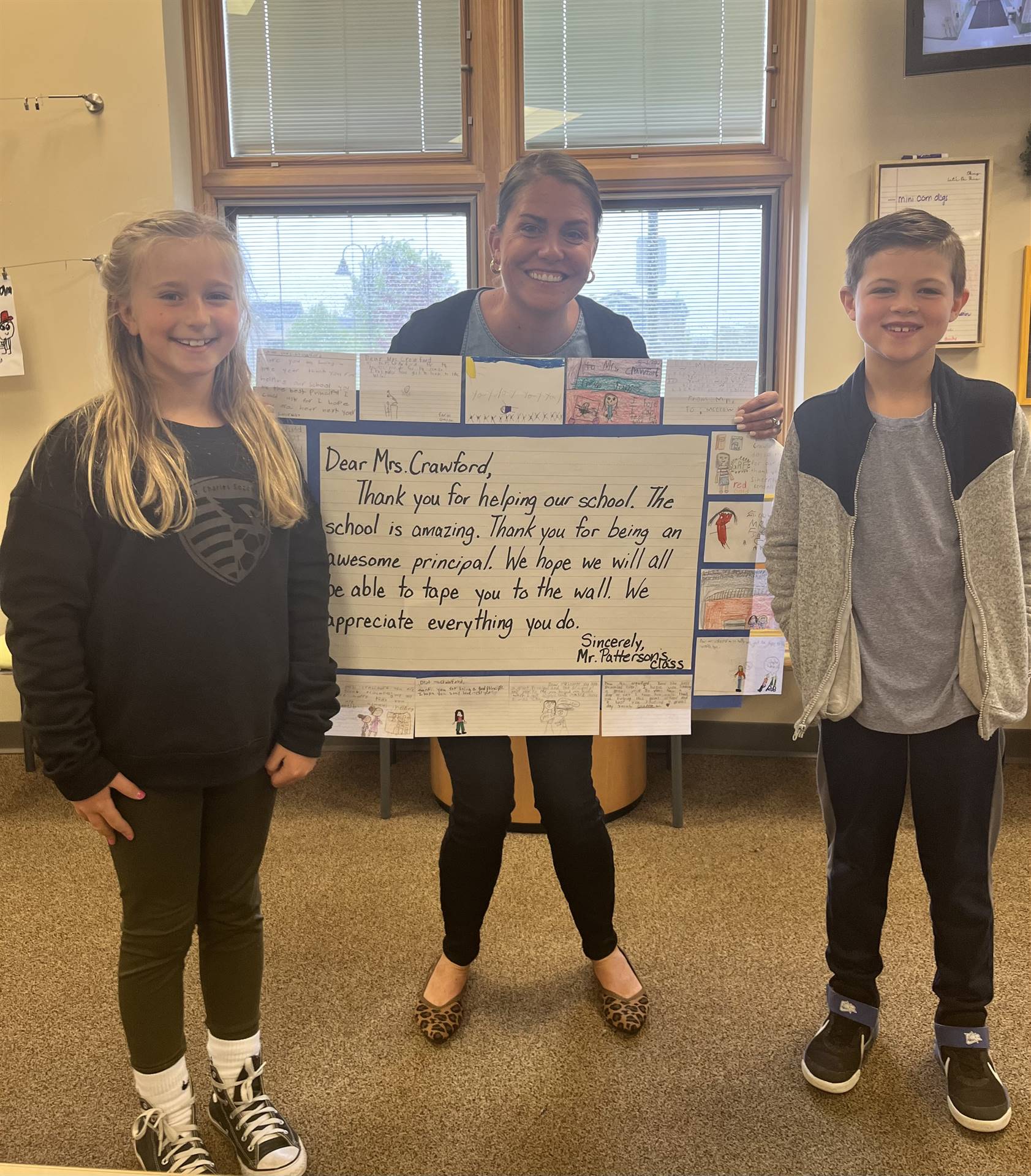 Principal Crawford and two students show poster of appreciation on Principal's Day for our tireless 