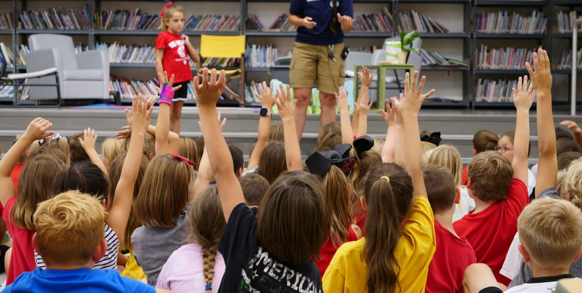 Many students raising their hands at a Prairie Run Elementary assembly