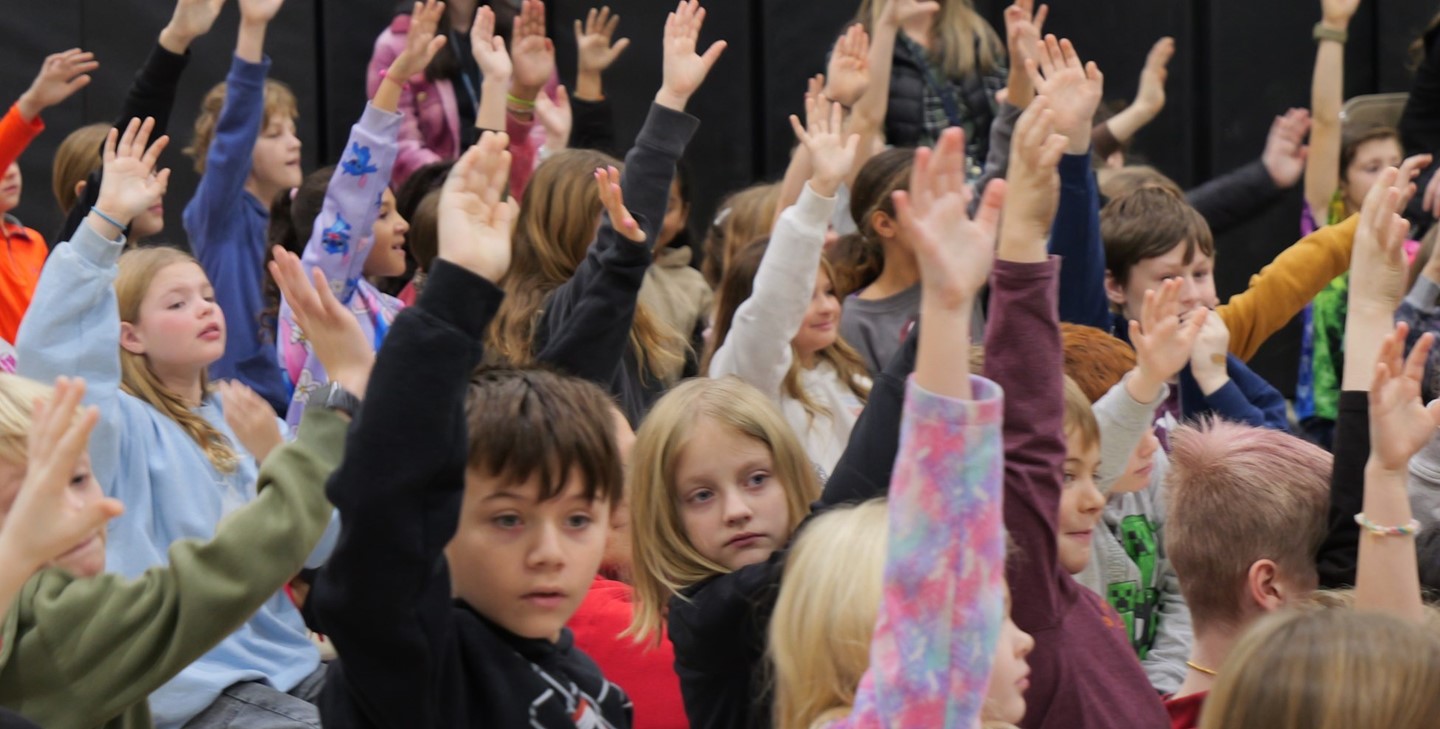 Students raise their hands at an assembly at Hylen Souders