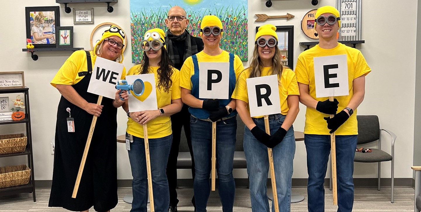 Teachers dressed up like Minions - holding signs that spell &#34;We Are PRE&#34; 