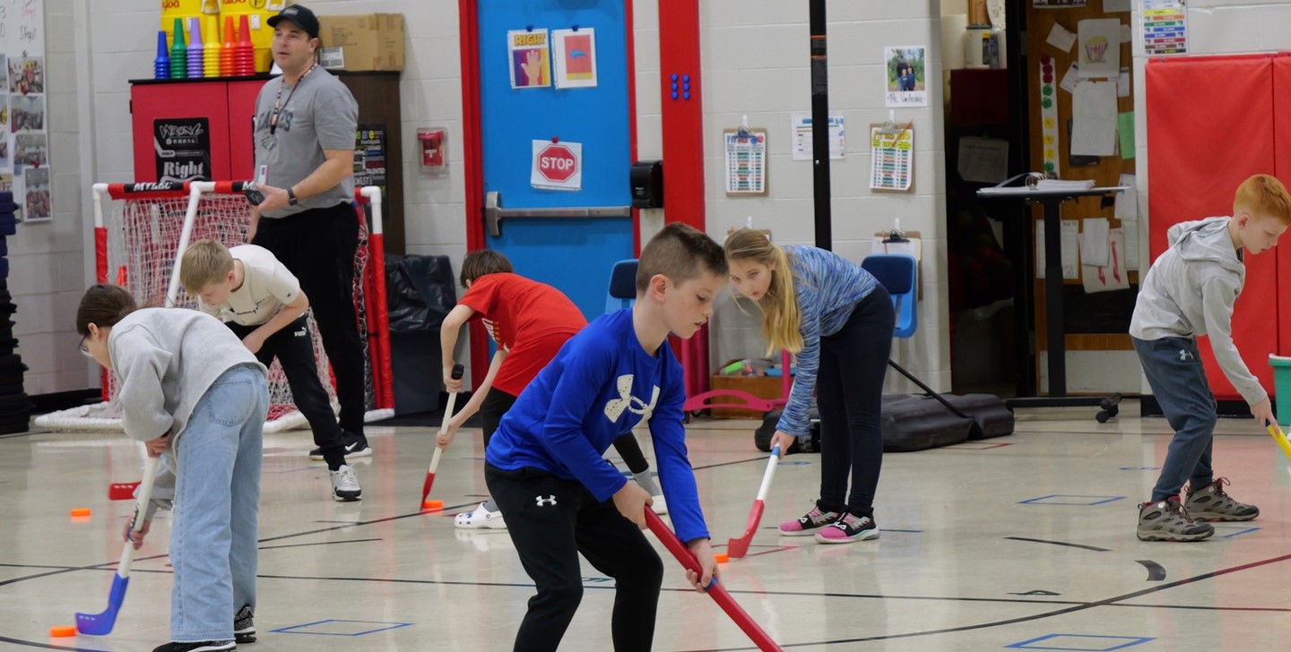 Students play foot hockey in gym class